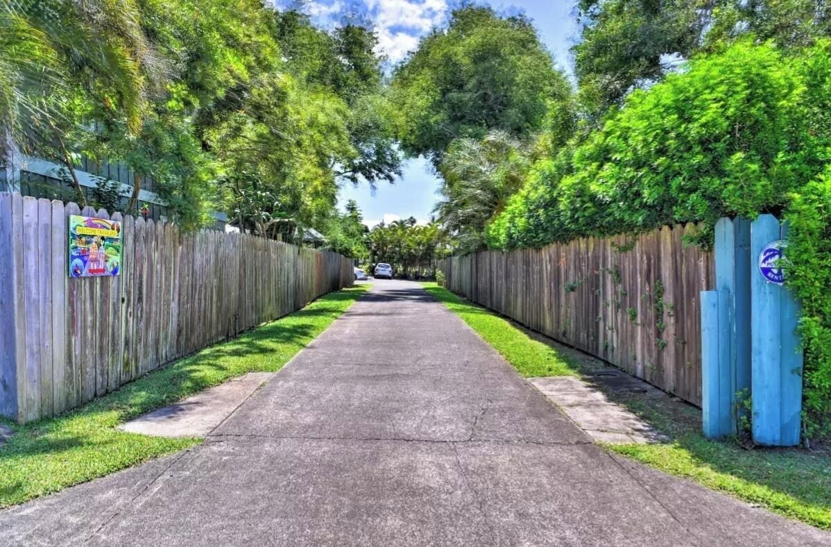 A paved pathway flanked by wooden fences with greenery overhead.