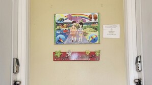 Un corridoio con un cartello fissato al muro che indica il divieto di fumare negli appartamenti, un tavolino decorato con un motivo floreale e un'opera d'arte colorata raffigurante una scena tropicale.