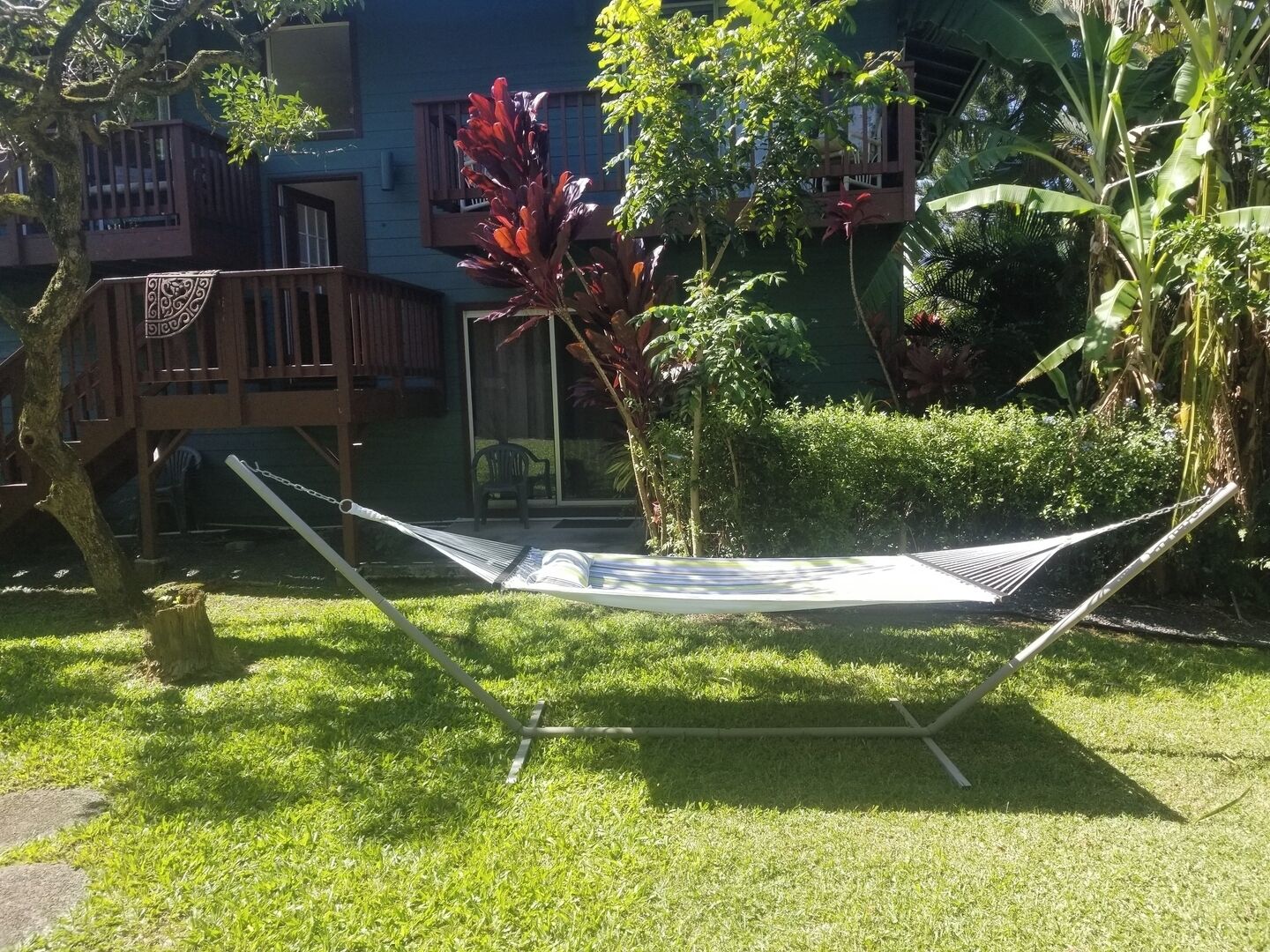 Uma rede em uma área gramada com um deck de madeira e um prédio ao fundo.