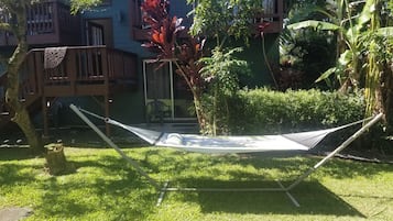 Uma rede em uma área gramada com um deck de madeira e um prédio ao fundo.