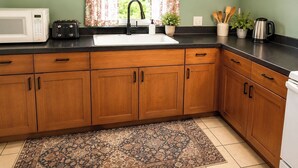 Una cocina con armarios de madera, microondas, pileta y ventana con cortinas florales.