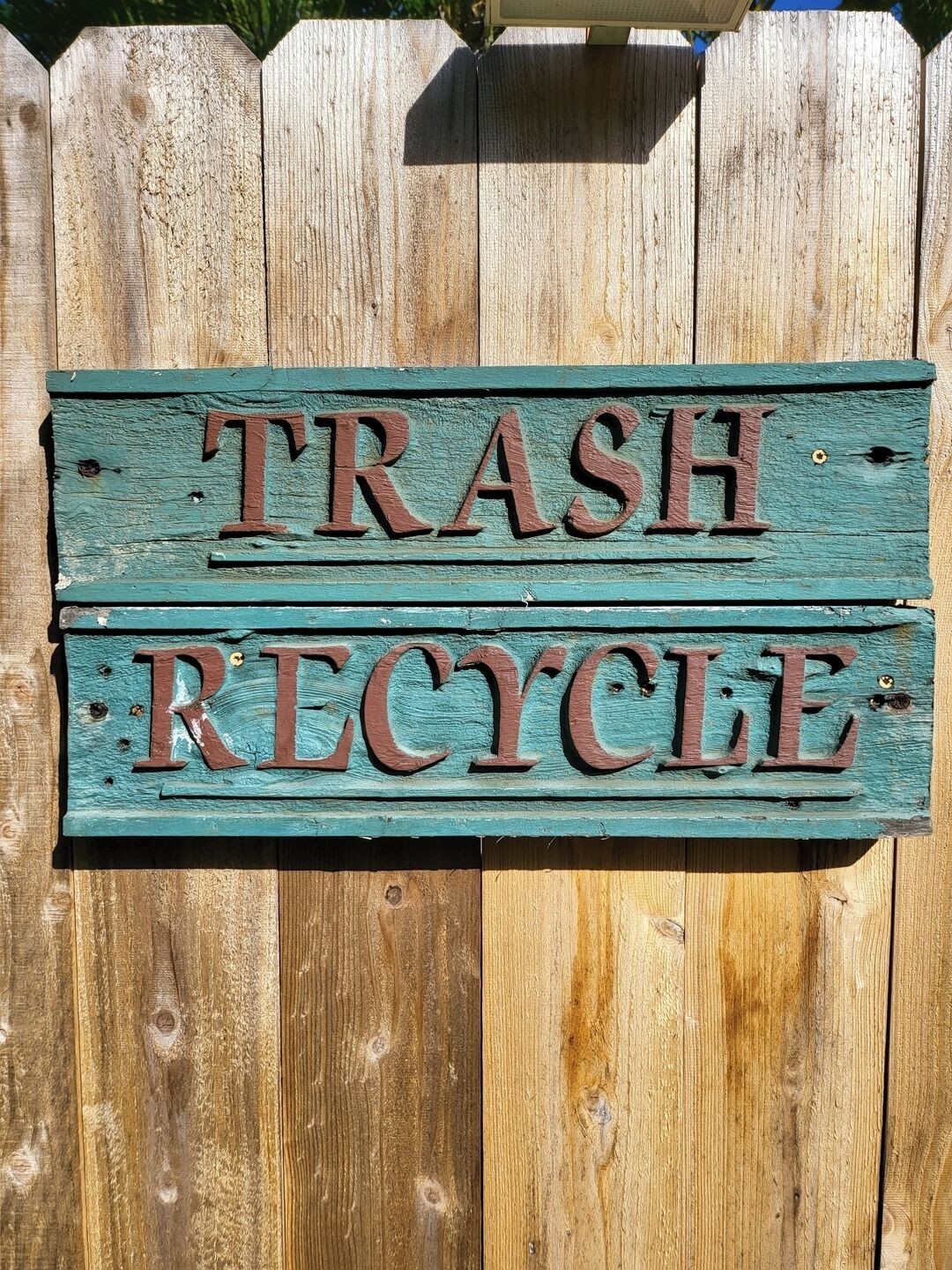 A wooden sign with the words 'TRASH RECYCLE' mounted on a fence.