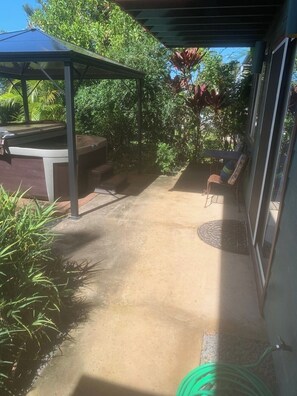 A covered outdoor area with a patio table and chairs, surrounded by lush greenery. - Private Hot Tub • Lanai + Full Kitchen (Haiku-Pauwela)