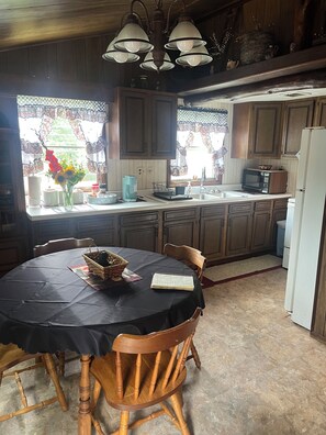Una cocina con armarios de madera, una mesa de comedor con sillas, un refrigerador y una ventana con cortinas.