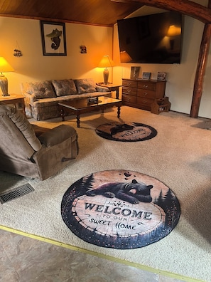 A cozy living room with a sofa, coffee table, and a fireplace. There are two welcome mats on the carpet. - Adorable 2-bedroom lake house with Lake Access near Confluence (Confluence)