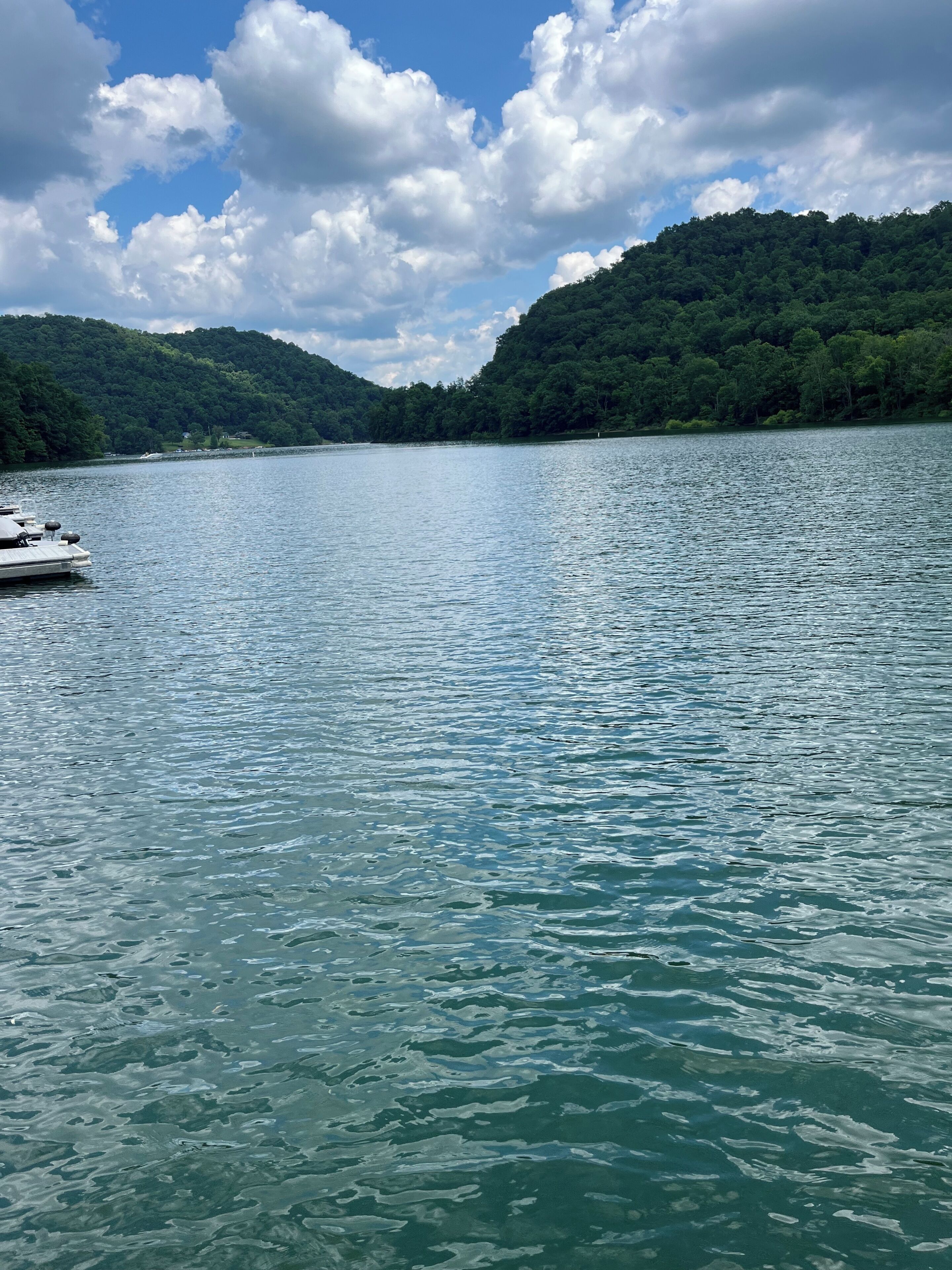 Un lago tranquilo con un bote amarrado a la izquierda, rodeado de colinas boscosas.