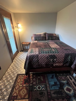 A bedroom with a bed, a nightstand, a floor lamp, and a patterned rug. - Adorable 2-bedroom lake house with Lake Access near Confluence (Confluence)