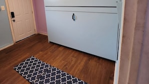 Et værelse med en stor, hvid garderobe, trægulv, et tæppe med et mønster og en dør med lyskontakt.