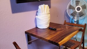 Et træspisebord med en fjernbetjening, et hvidt håndklæde og et TV ophængt på væggen.
