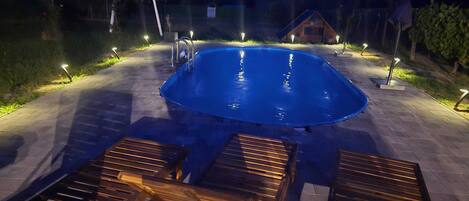 An outdoor swimming pool with a wooden deck and lounge chairs.