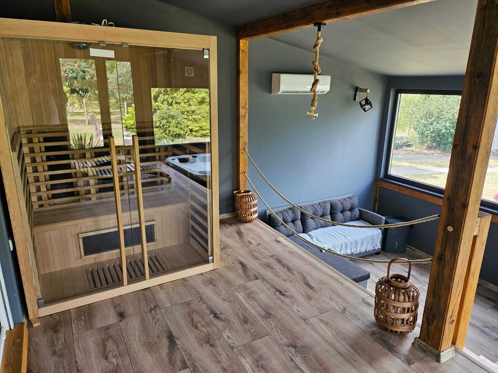 Un intérieur moderne avec un plancher en bois, une véranda en verre avec un jacuzzi, un hamac et un luminaire suspendu.