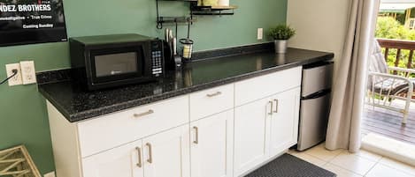 A kitchen with white cabinets, a black countertop, a microwave, and a dish rack.