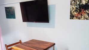 Een kamer met een houten tafel, twee stoelen, een aan de muur bevestigde televisie en een stopcontact.