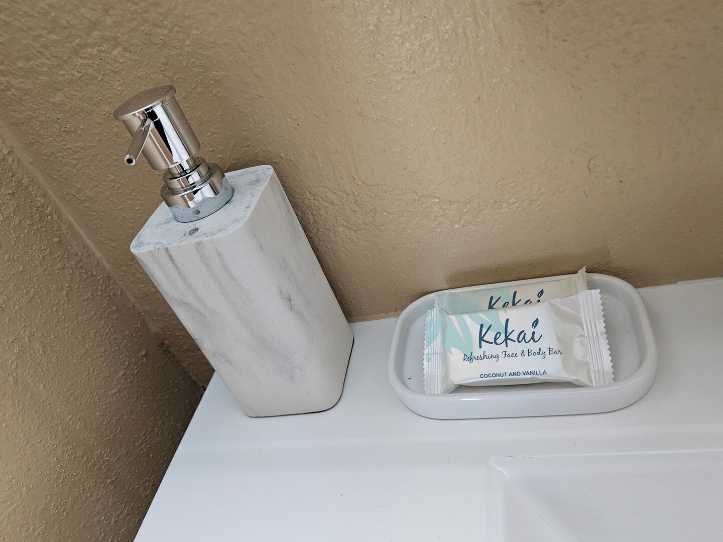 A bathroom with a marble soap dispenser and a bar of Kekaï coconut and vanilla soap.