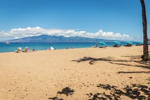 A beach with clear skies, a mountain range in the background, and several umbrellas and lounge chairs. - Downtown Wailuku Studio • Queen Bed + AC (Wailuku)