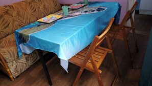 Ein Essbereich mit Tisch, bedeckt mit einer blauen Tischdecke, Holzstühlen und einem gemusterten Sofa.