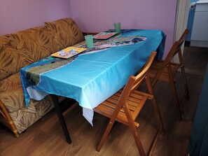 A dining area with a table covered by a blue tablecloth, wooden chairs, and a patterned sofa. - Downtown Wailuku Studio • Queen Bed + AC (Wailuku)