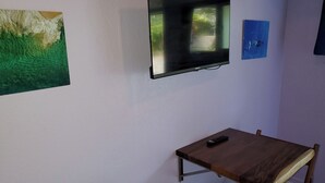 Una habitación con una televisión en la pared, una mesita con un control remoto y una silla.