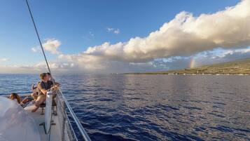 A boat with passengers enjoying the view of the sea and a distant rainbow.