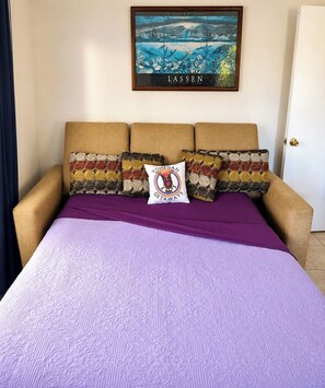 A bed with a purple bedspread and patterned pillows, a framed picture above the bed, and a door to the right. - Private Haiku Stay • Full Kitchen + Parking (Haiku-Pauwela)