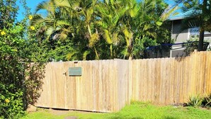 Een omheinde tuin met gazon, een palmboom en een houten schutting.