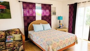 Een slaapkamer met een bed, nachtkastje, lamp, bank en raam met gordijnen.
