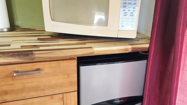 Een kleine keuken met een magnetron, een koelkast en houten kastjes.
