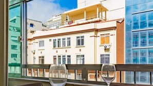 Una mesa de comedor con dos copas de vino y platos, adornada con individuales rojos, en una habitación con vistas a un edificio a través de una ventana.