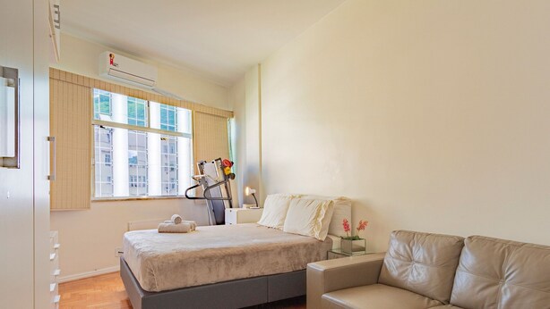 Un dormitorio con cama, mesita de noche, lámpara, sofá y ventana con persianas.