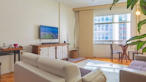 Una sala de estar con un sofá, una mesa de centro, un televisor montado en la pared y una ventana con persianas.