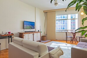 Ein Wohnzimmer mit einer Couch, einem Couchtisch, einem an der Wand montierten Fernseher und einem Fenster mit Jalousien.