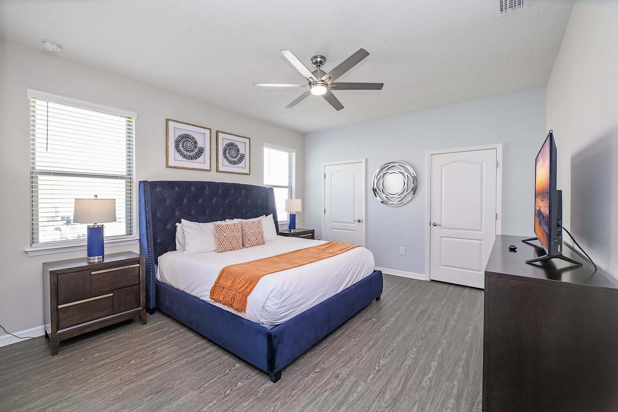 A bedroom with a bed, nightstands, a ceiling fan, a TV, and artwork on the walls.