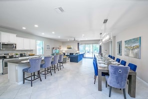 A modern kitchen with white cabinets, a microwave, and a dining area with blue chairs and a wooden table. - Soak Up the Sun! Luxury 8BR Villa & South Pool (Kissimmee)