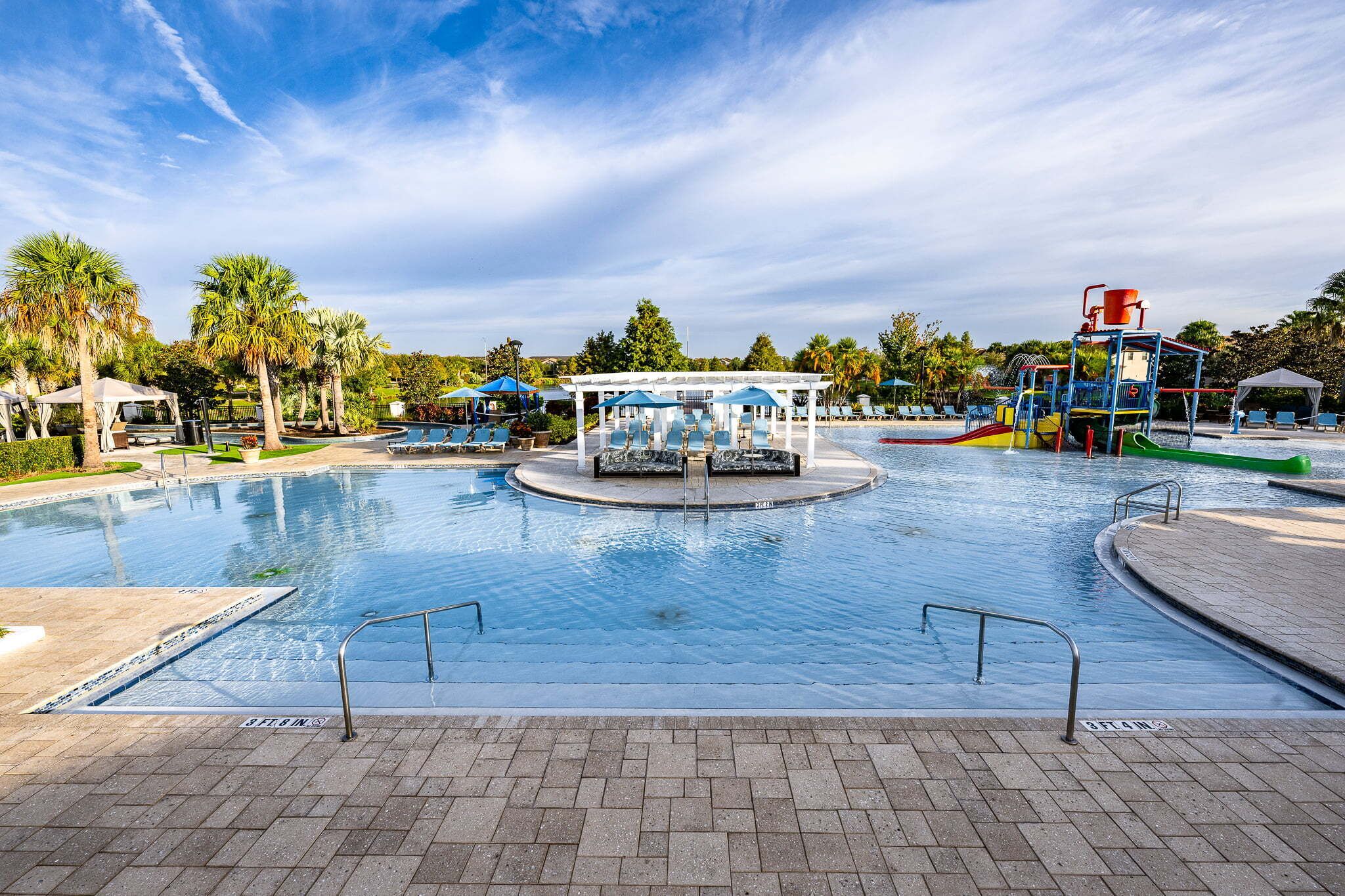 A swimming pool with a water slide, lounge chairs, and a pavilion.