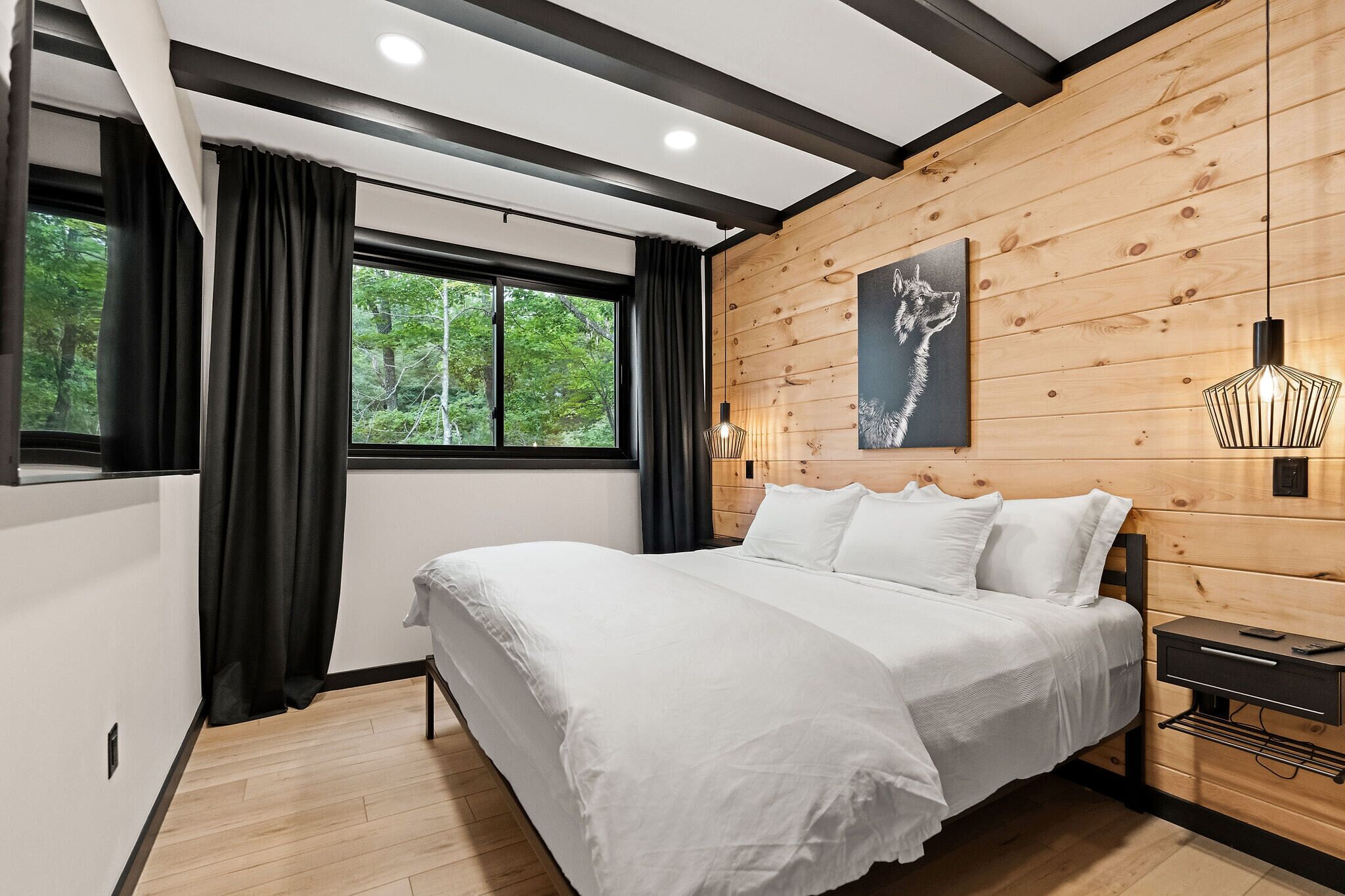 Une chambre avec un grand lit, une fenêtre avec des rideaux, un mur en bois et un tableau.
