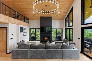 Un salon moderne avec un grand canapé d’angle, une cheminée et un fauteuil suspendu.