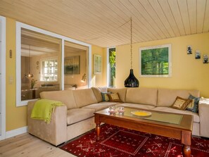 A living room with a beige sofa, a glass coffee table, and a red patterned rug. There is a large window with a view of greenery outside. - "Lonneke" -  from the sea by Interhome (Hals)