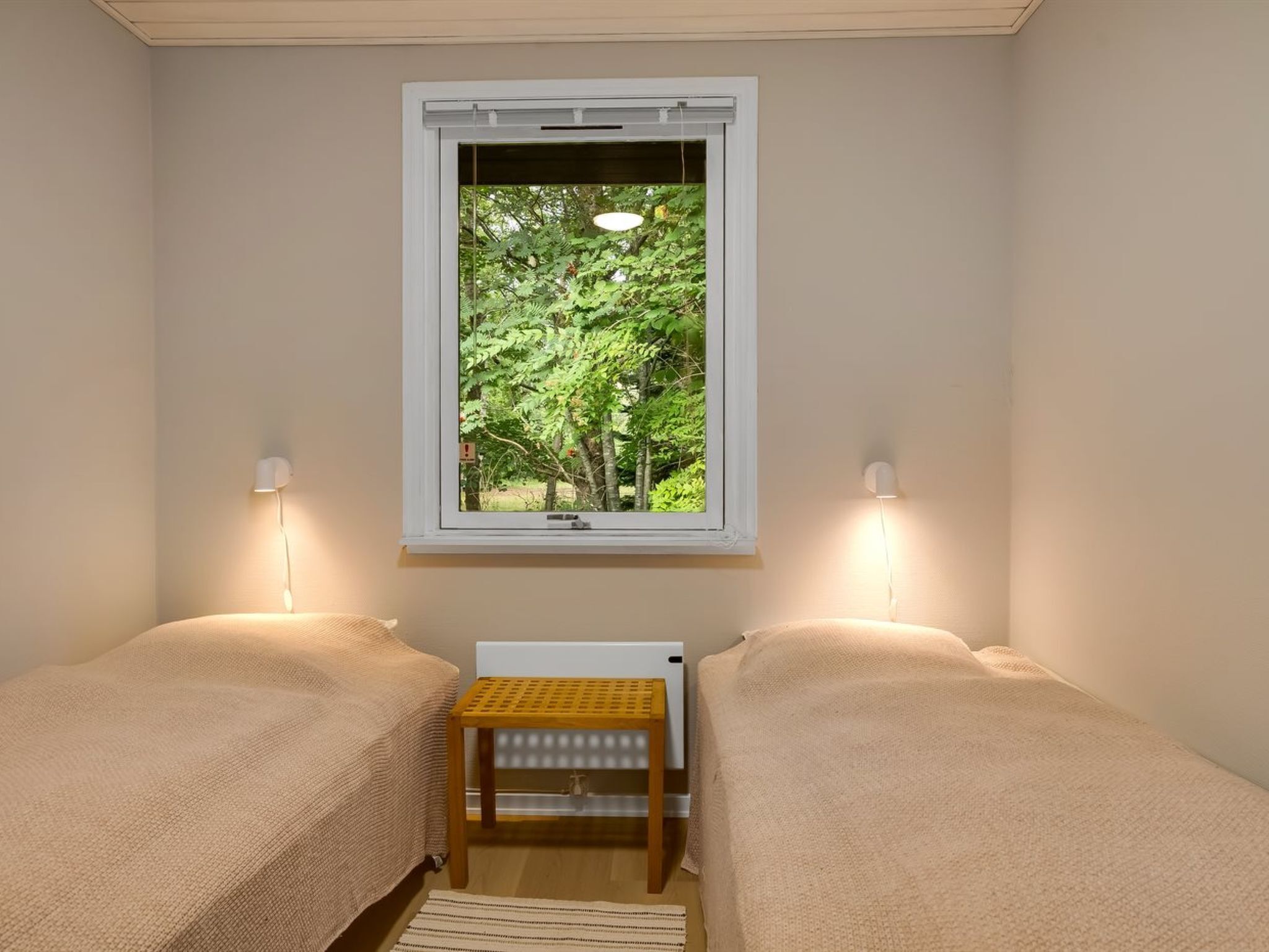 A room with two beds, a radiator, and a window with a view of trees.