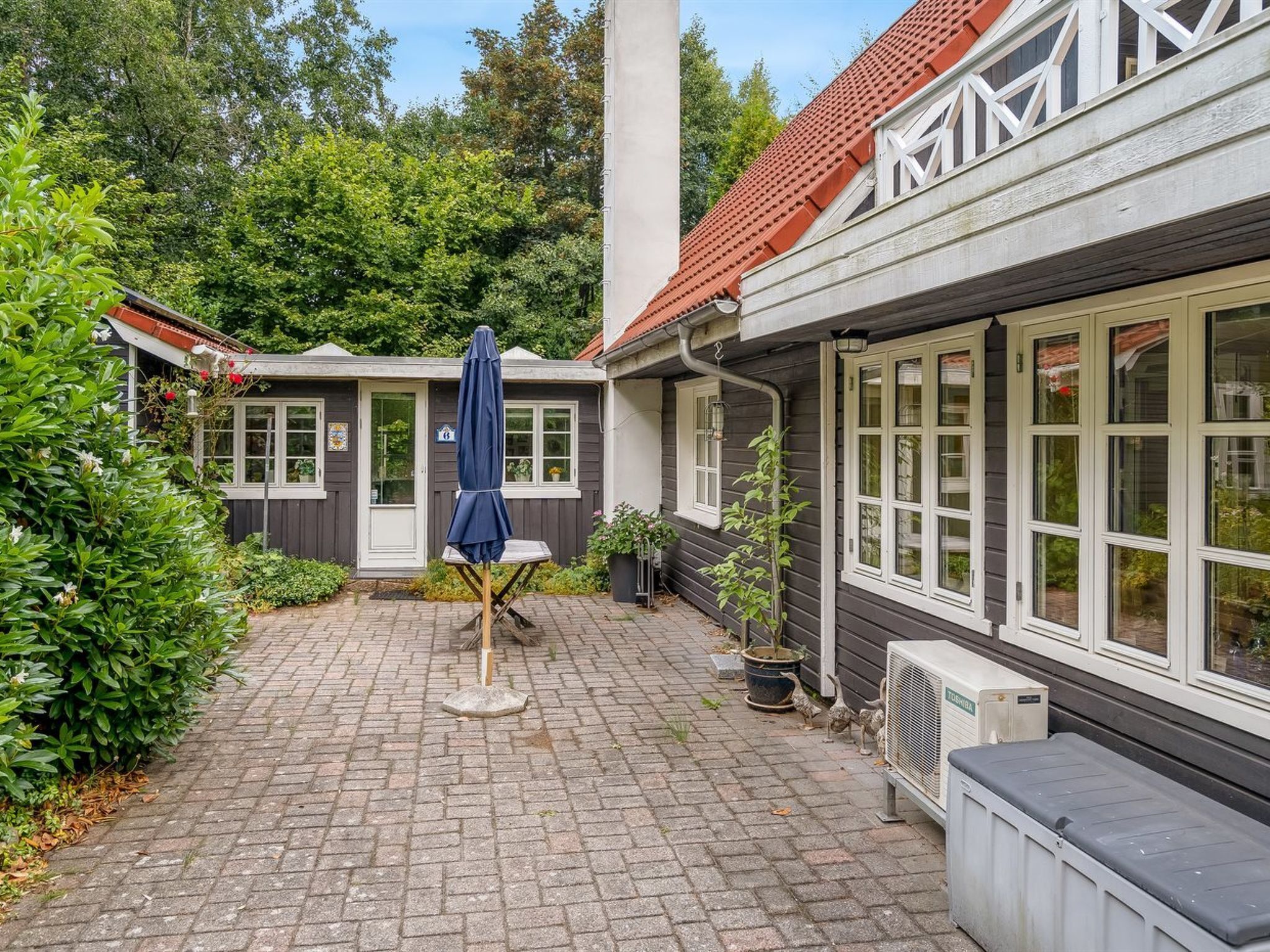 A courtyard with a brick floor, a blue umbrella, and a white air conditioning unit.