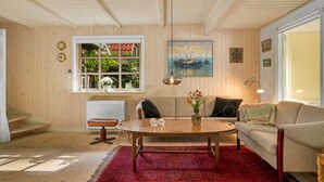 Una sala de estar acogedora con piso de madera, un tapete rojo estampado, una mesa de centro de madera, un sofá y una ventana con vistas a la vegetación.
