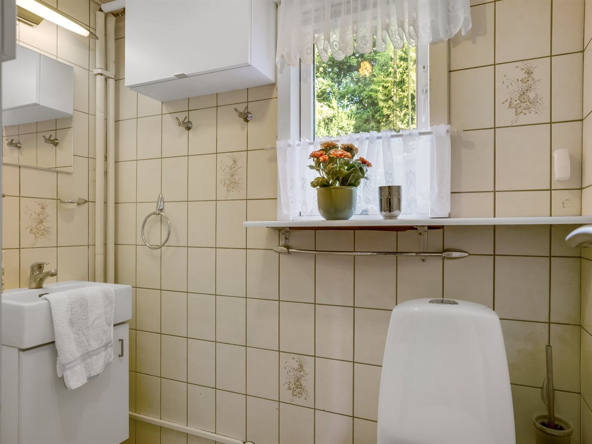 A bathroom with a toilet, sink, and window with a view of greenery.
