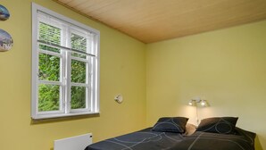 Un dormitorio con cama, ventana, radiador y una lámpara fijada a la pared.