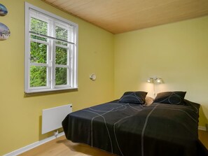 Ein Schlafzimmer mit Bett, Fenster, Heizkörper und einer Wandleuchte.