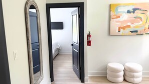 A hallway with a mirror, a bed, a fire extinguisher, and ottomans. - The Clark House St. Augustine (Saint Augustine)