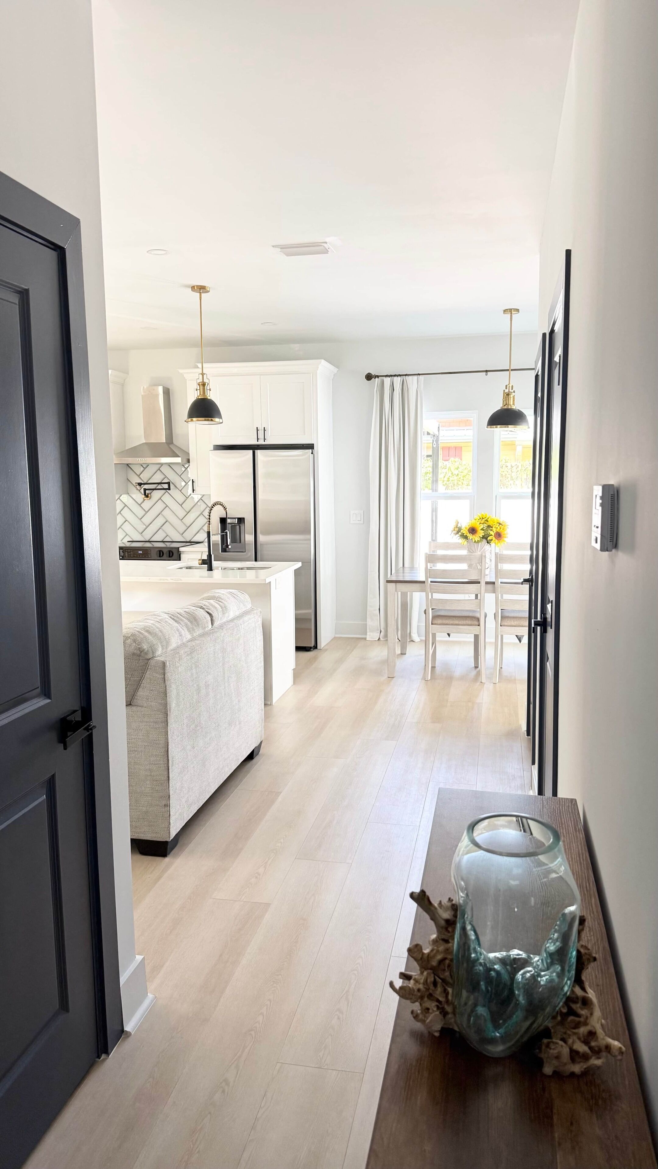 Une cuisine moderne dotée d’un îlot central, d’un coin repas avec une table et des chaises, et d’un couloir menant à une porte.