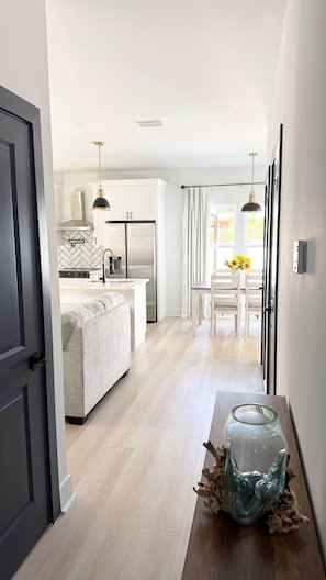 A modern kitchen with a central island, a dining area with a table and chairs, and a hallway leading to a door. - The Clark House St. Augustine (Saint Augustine)