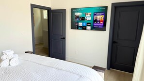 Ein Hotelzimmer mit einem Bett, einem an der Wand befestigten Fernseher, der Streaming-Dienste anzeigt, und einer Tür zu einem anderen Raum.
