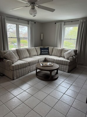 A living room with a sectional sofa, a round coffee table, and a ceiling fan. - High Tide Hideaway - 3-bedroom house in Sagamore Beach walking distance to beach (Bourne)
