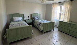 Une chambre à coucher avec deux lits verts, une table de chevet, une commode et une fenêtre avec des rideaux.