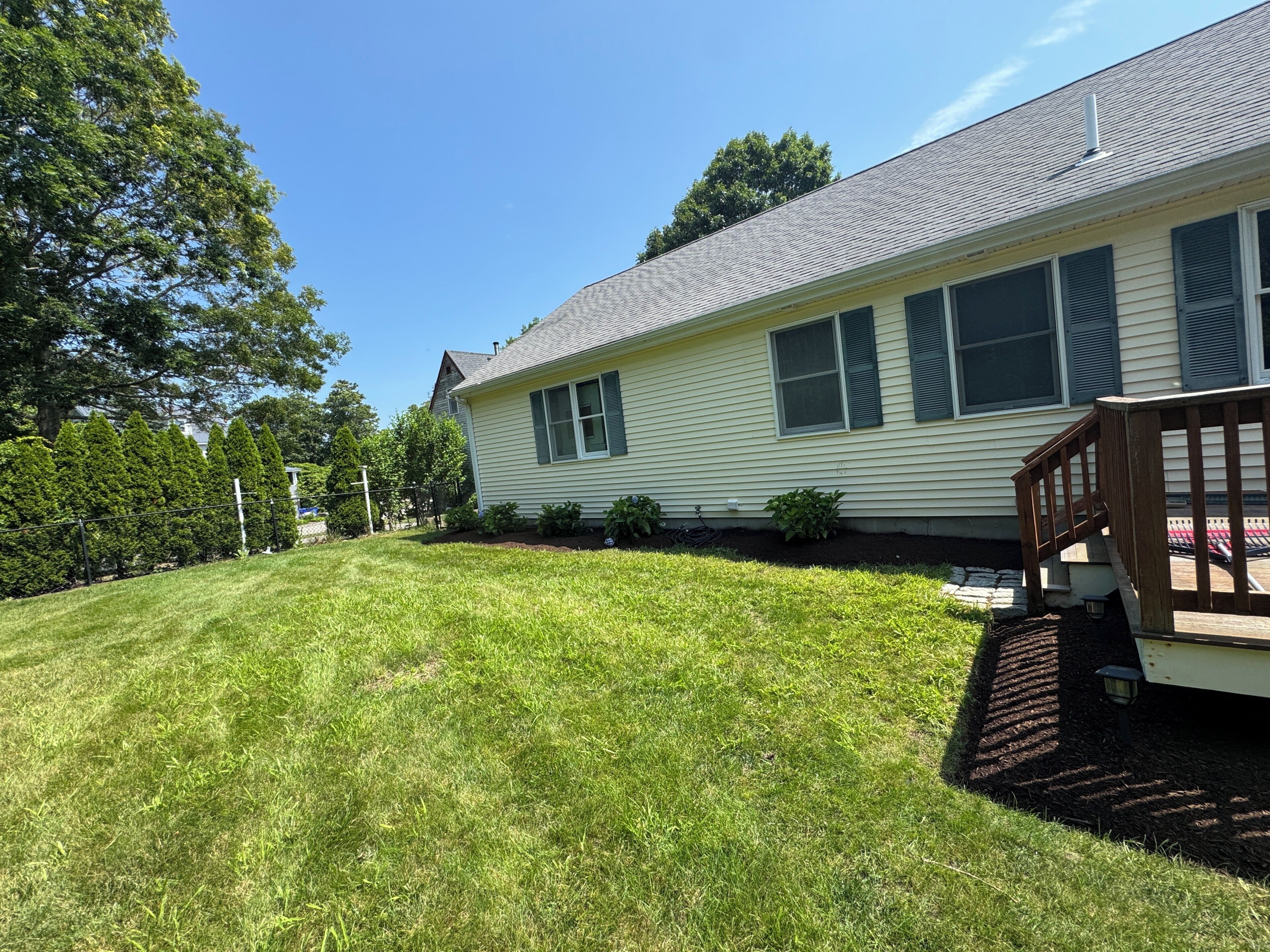 A residential house with a well-maintained lawn, a wooden deck, and a clear sky.